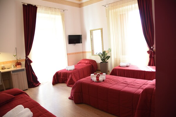 Habitación de hotel con tres camas, televisión, escritorio y una planta en maceta.