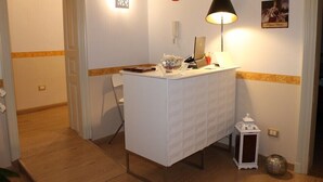 A small, white, covered desk with a lamp, a red decorative item, and a framed picture on the wall. - B&B The Queens (Foggia)