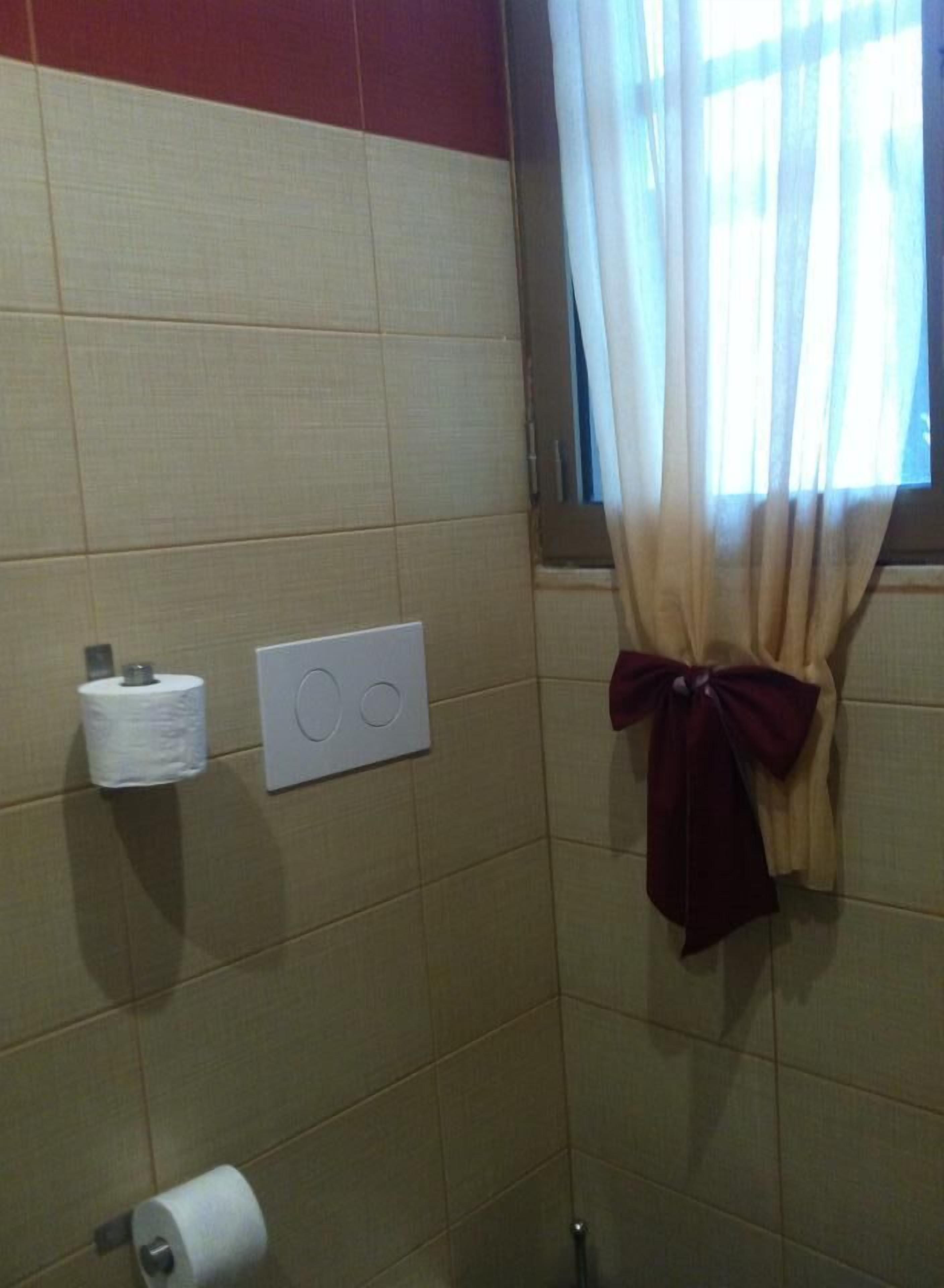 Ein Badezimmer mit beigen Fliesen, einem Toilettenpapierhalter, einem Lichtschalter und einem Handtuch mit Schleife.
