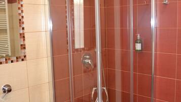 A glass-enclosed shower with a handheld showerhead, a glass sink, and a mirror with a mosaic border.