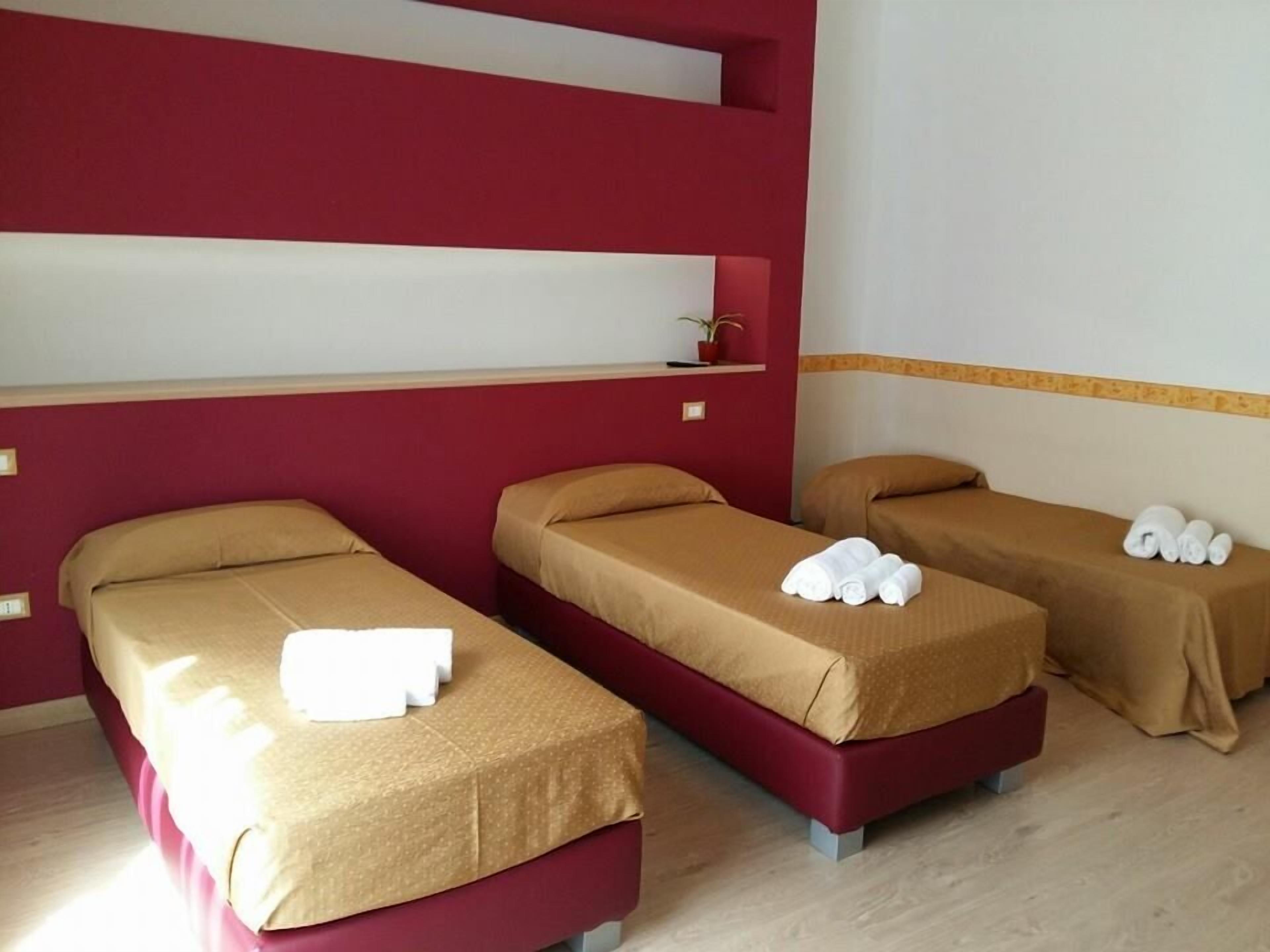 Habitación de hotel con tres camas individuales, cada una con cubrecama marrón y toallas blancas.