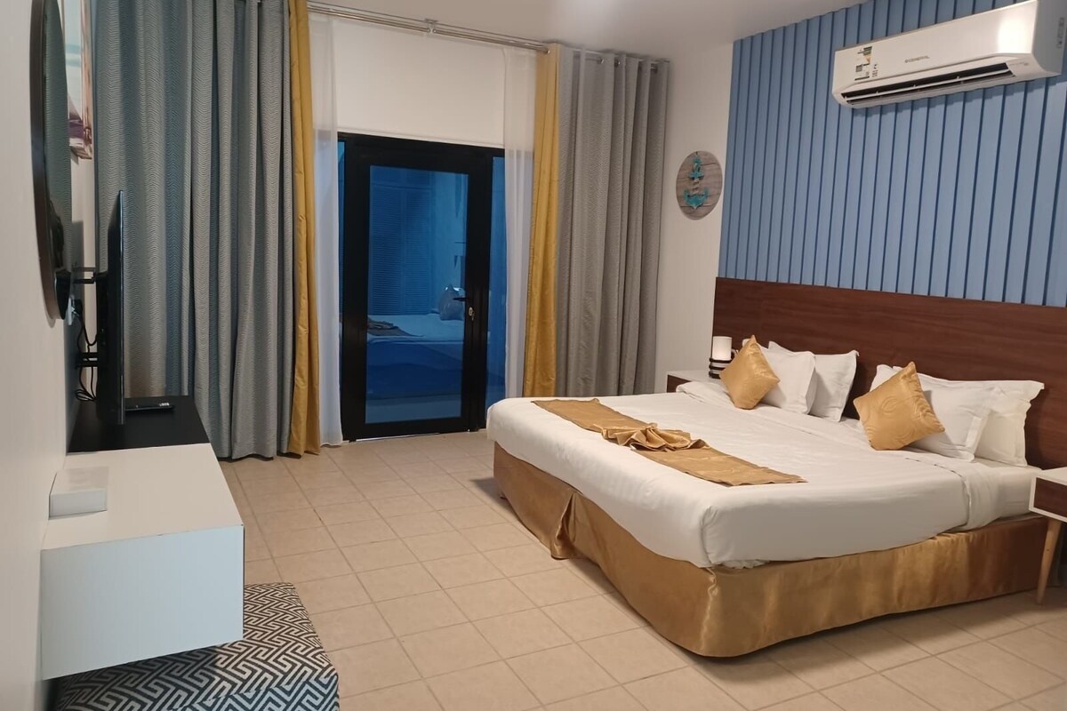 Ein Hotelzimmer mit Bett, Nachttischen, einer Klimaanlage, einem Fernseher und Blick durch eine Glastür.