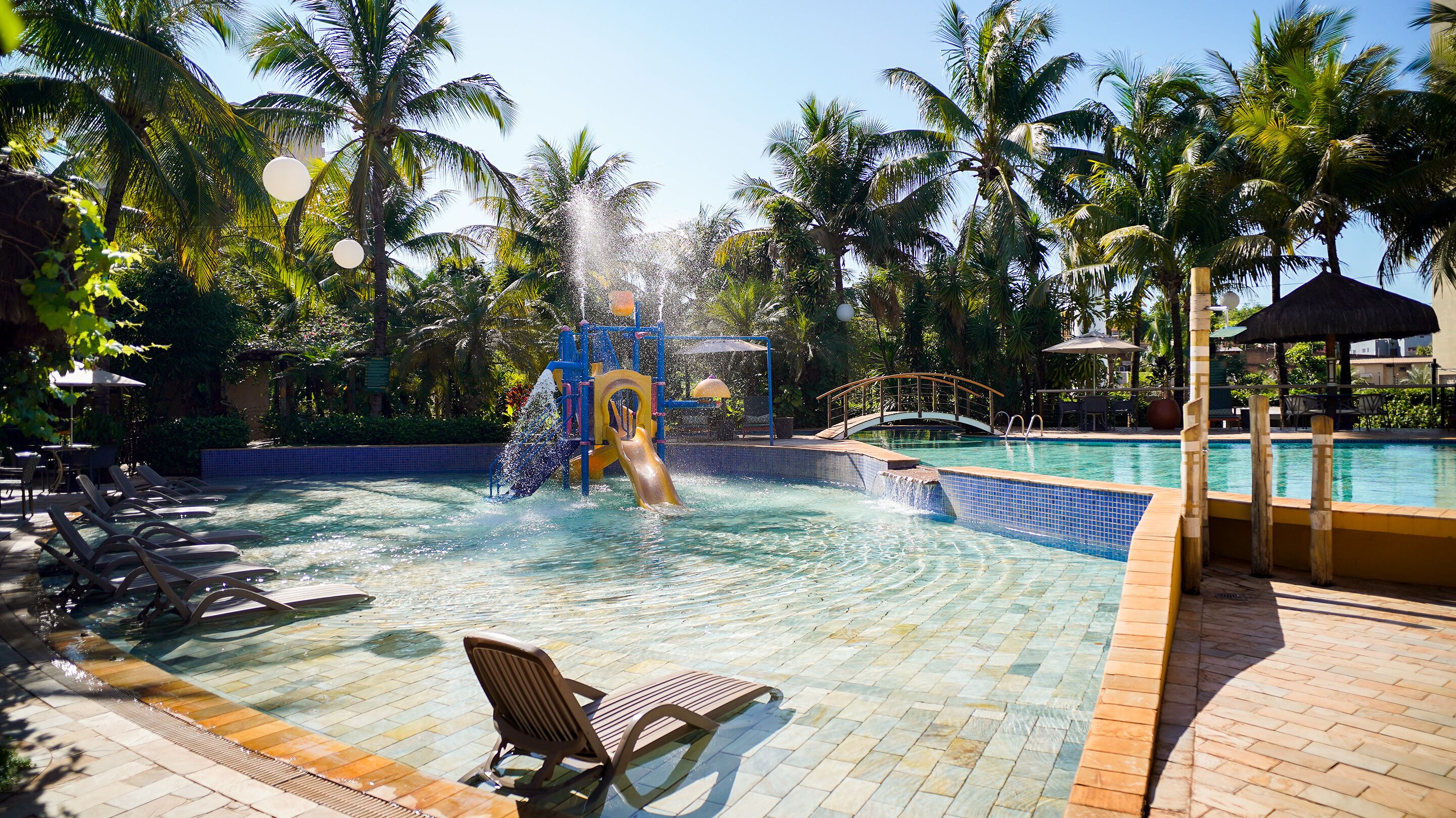 Une piscine avec un toboggan, des chaises longues et des palmiers.
