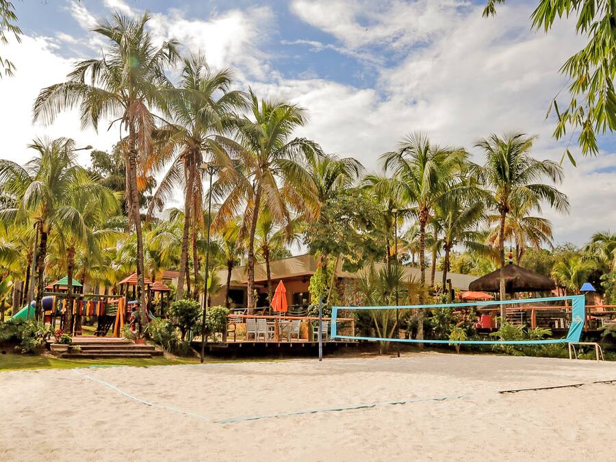 Una cancha de voleibol de playa con palmeras y un parque infantil al fondo.