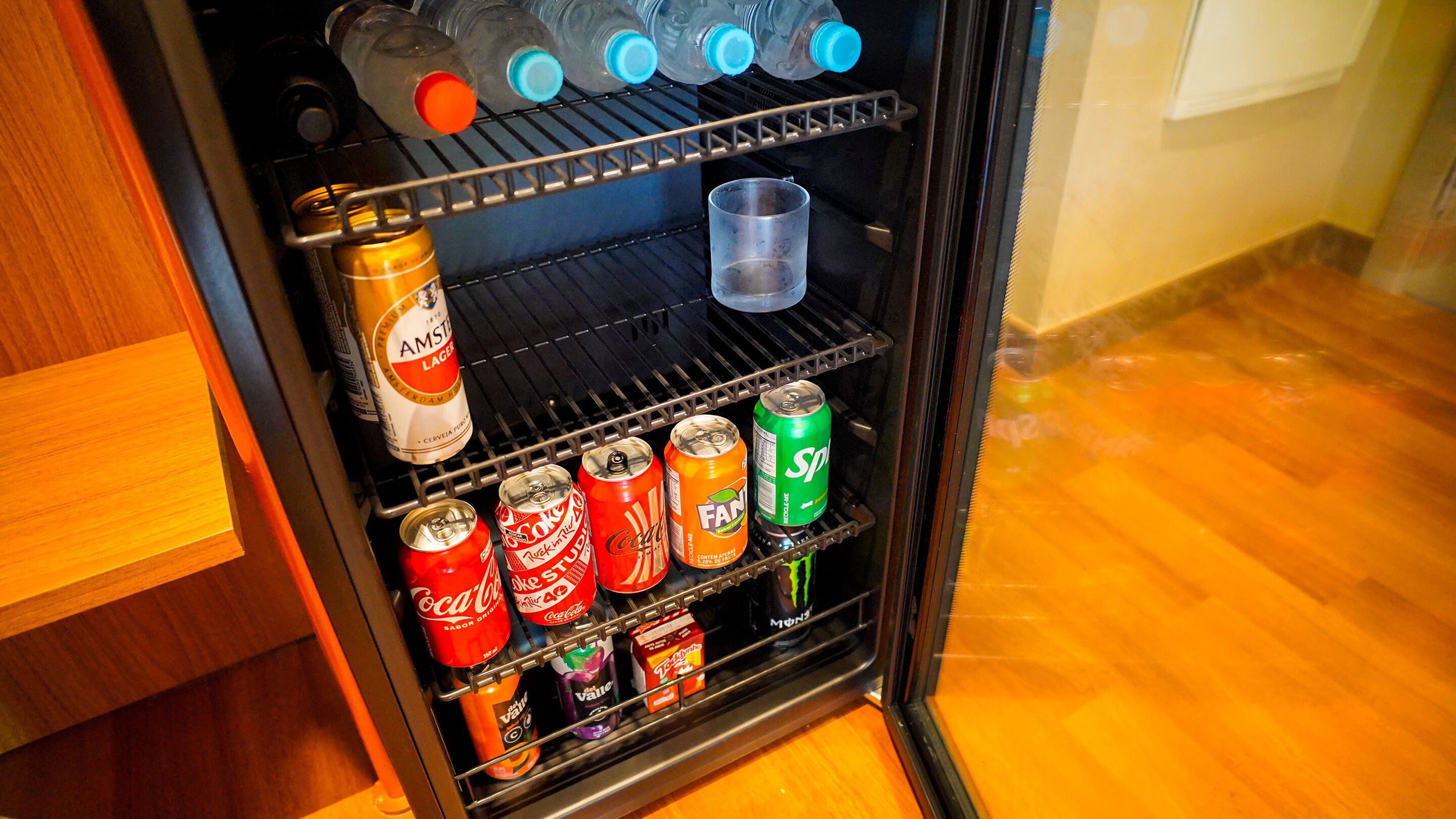 Mini-frigorífico com diversas bebidas, incluindo cerveja, refrigerantes e energéticos.