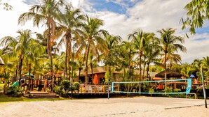 A beach volleyball court surrounded by palm trees and a playground. -  Hot Beach Raízes (Olímpia)