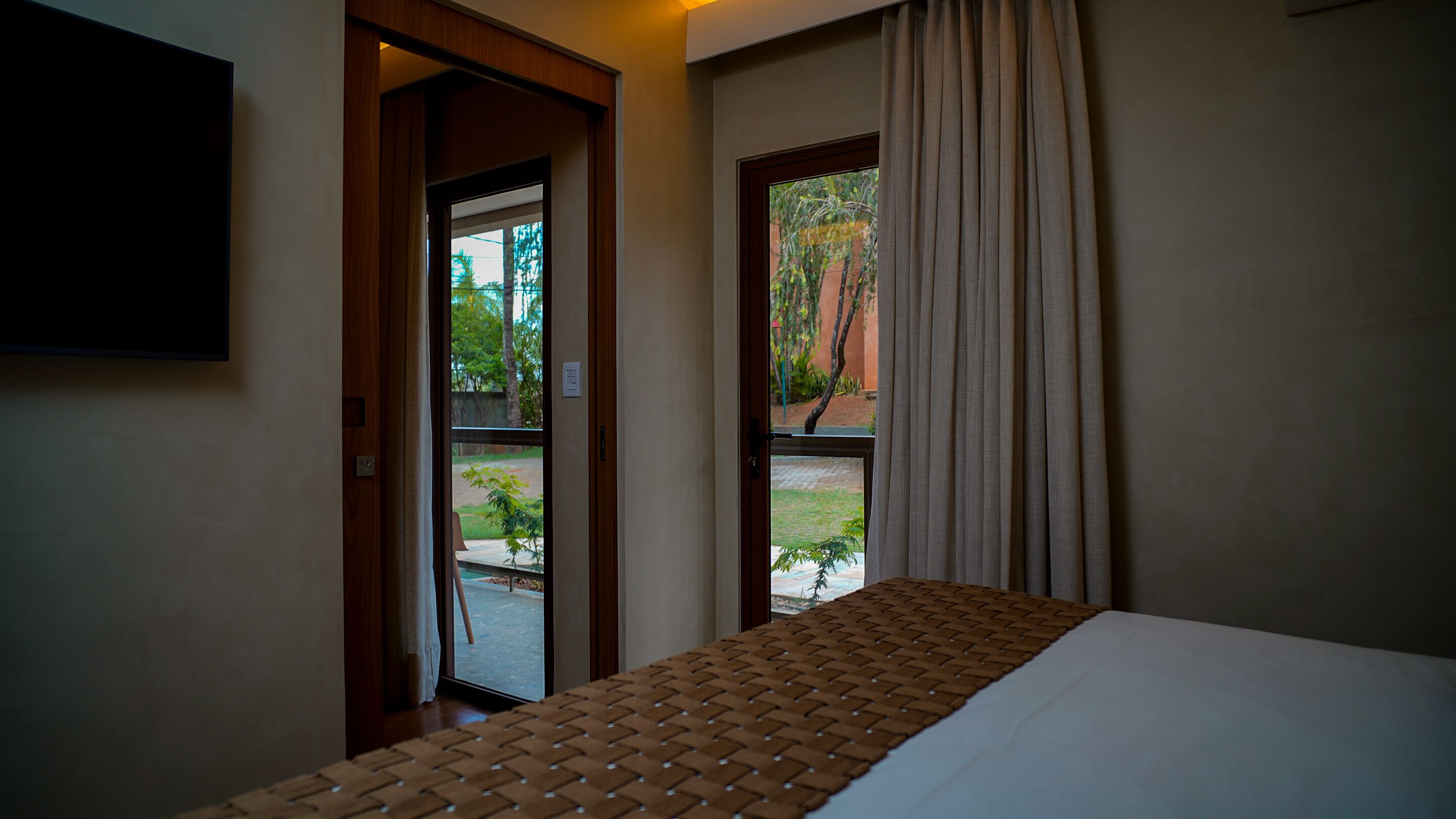 A hotel room with a bed, a window with curtains, and a view of the outdoors.