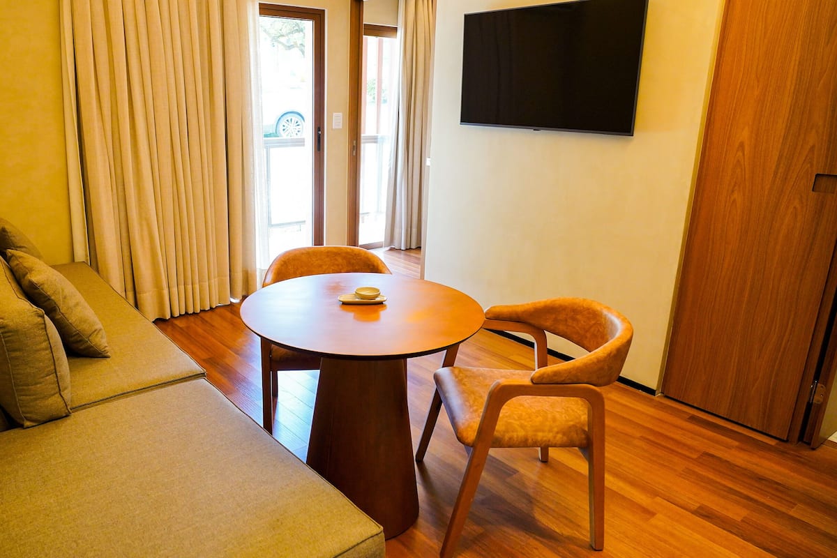 Ein modernes Wohnzimmer mit einer Couch, zwei Sesseln, einem runden Tisch und einem an der Wand befestigten Fernseher.