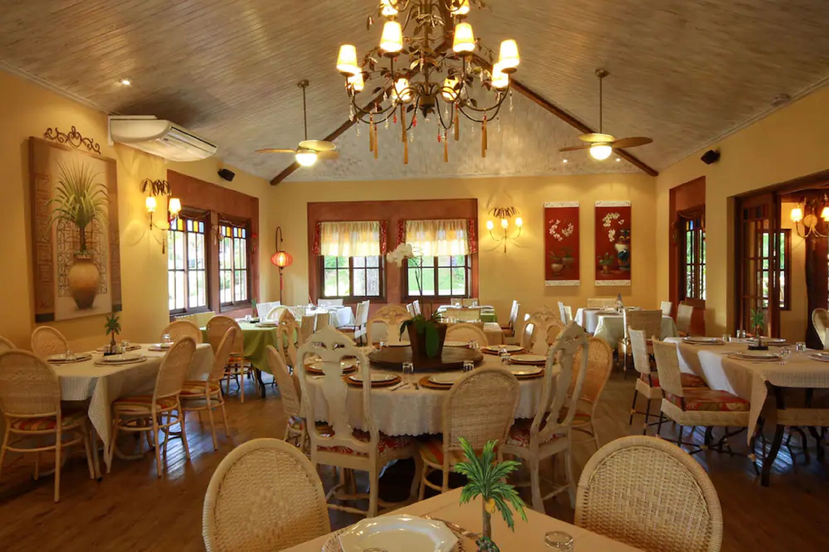 A spacious dining area with multiple tables and chairs, a chandelier, and large windows allowing natural light.