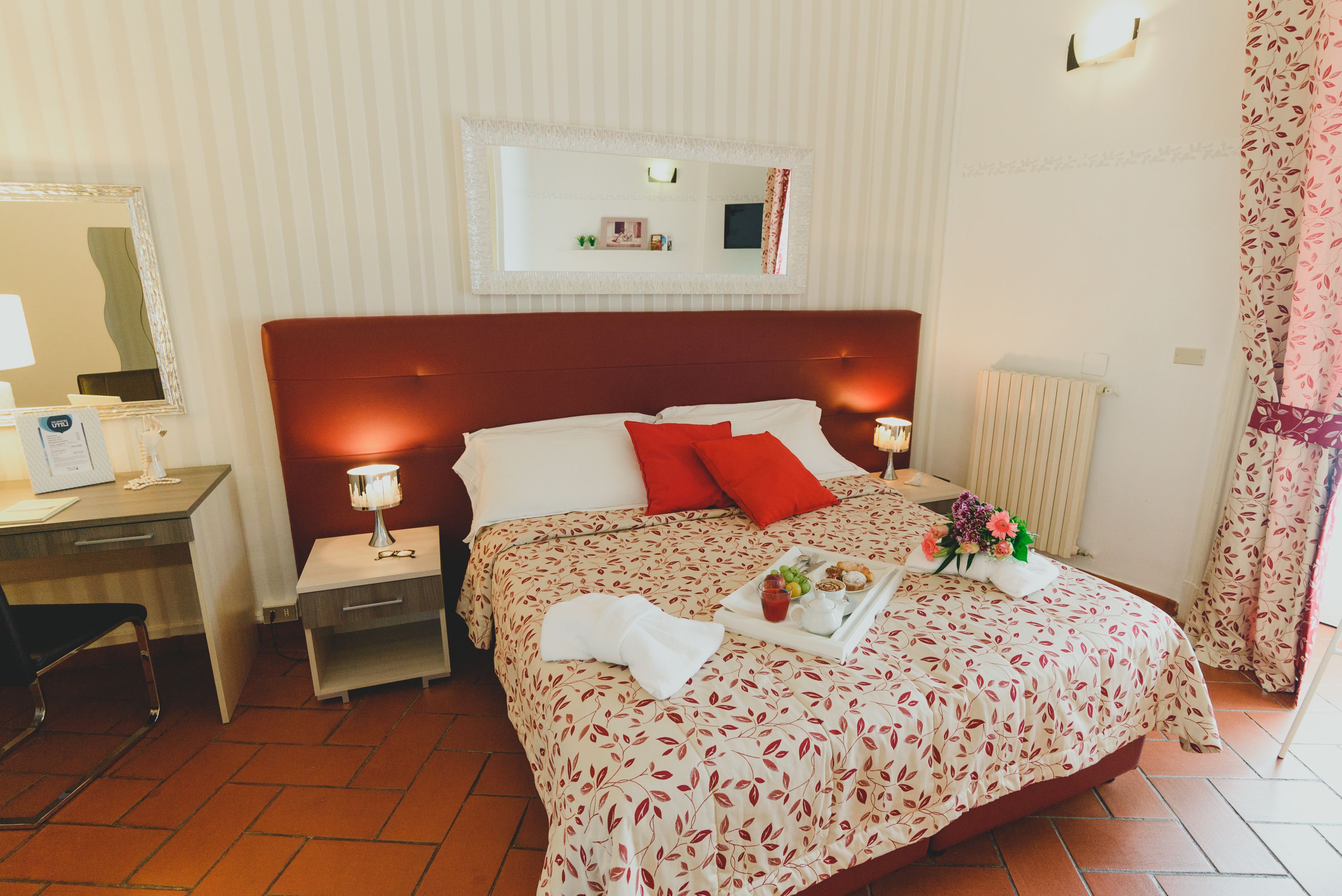 A hotel room with a large bed, a bedside table, a desk, and a mirror.