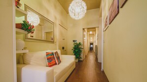 A hallway with a white sofa, a potted plant, and a chandelier. - Bellini Home B&B (Catania)
