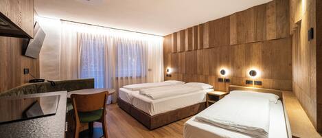 A hotel room with a wooden wall panel, two beds, a desk with a chair, and a window with curtains.