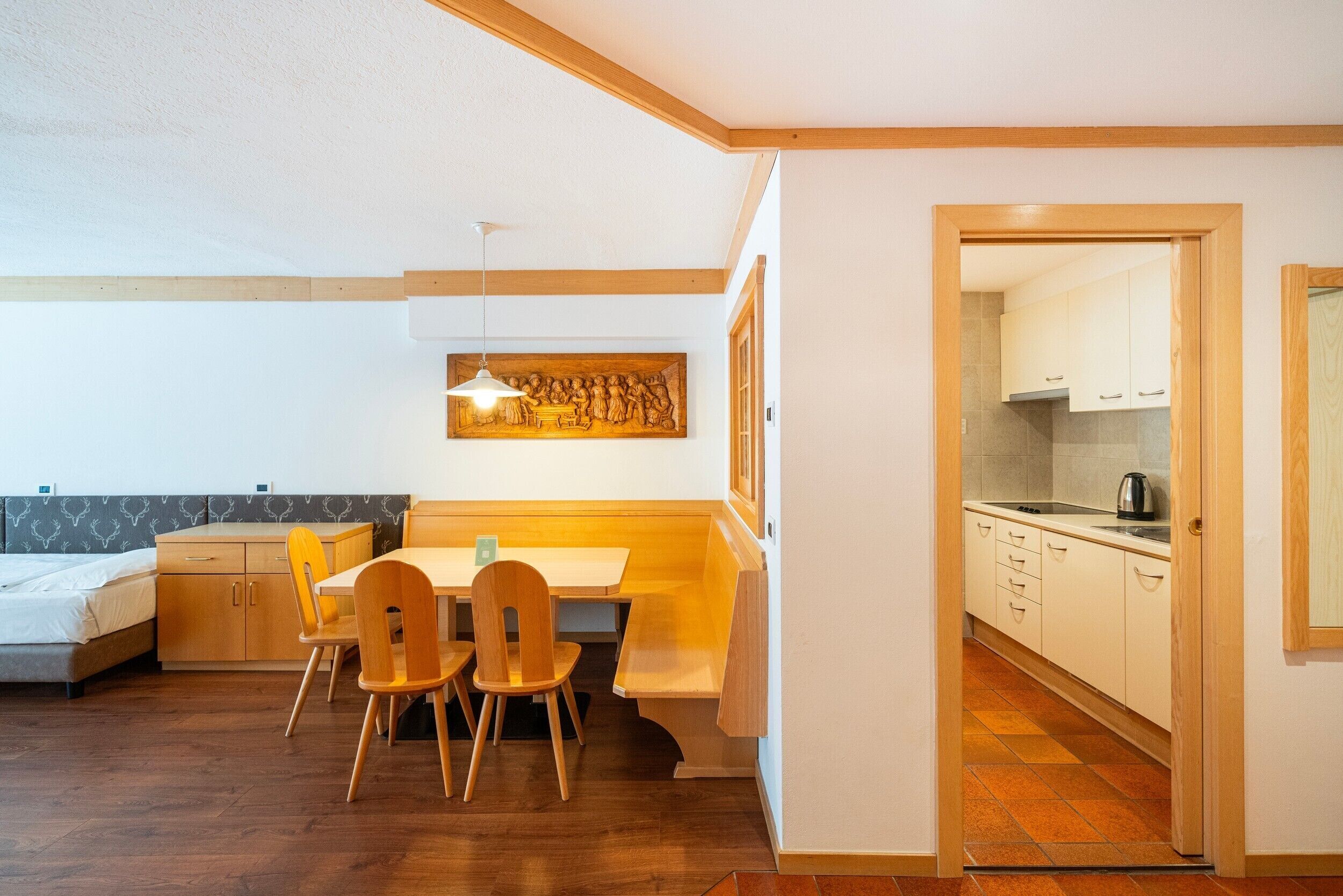 Een knus kamertje met een bed, een eettafel met stoelen, een kitchenette en een houten plafond.