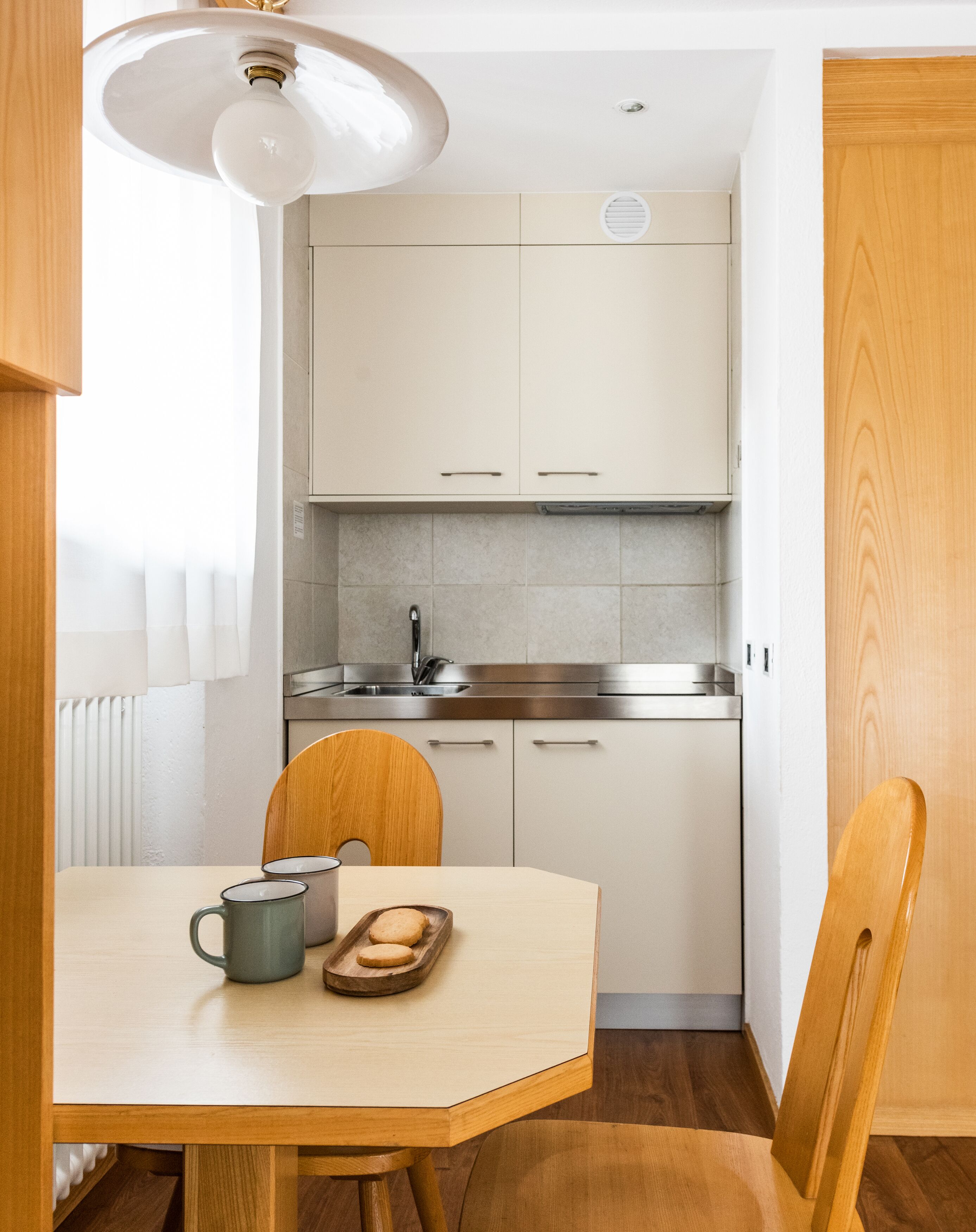 Una cocina compacta con armarios blancos, un lavamanos de acero inoxidable y una mesa de comedor de madera con sillas.