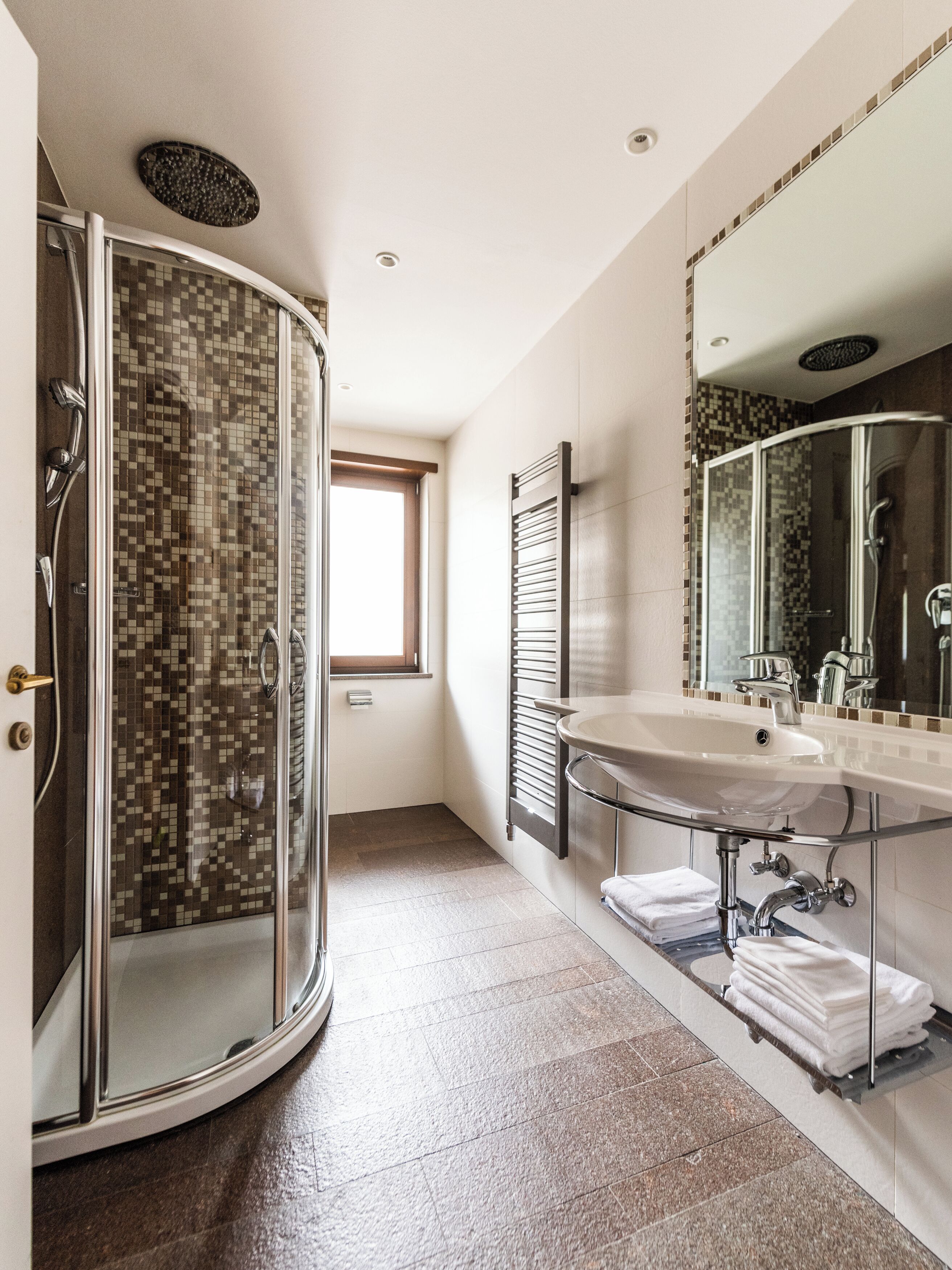 A modern bathroom with a glass-enclosed shower, a large mirror, and a vanity with a sink and towel rack.