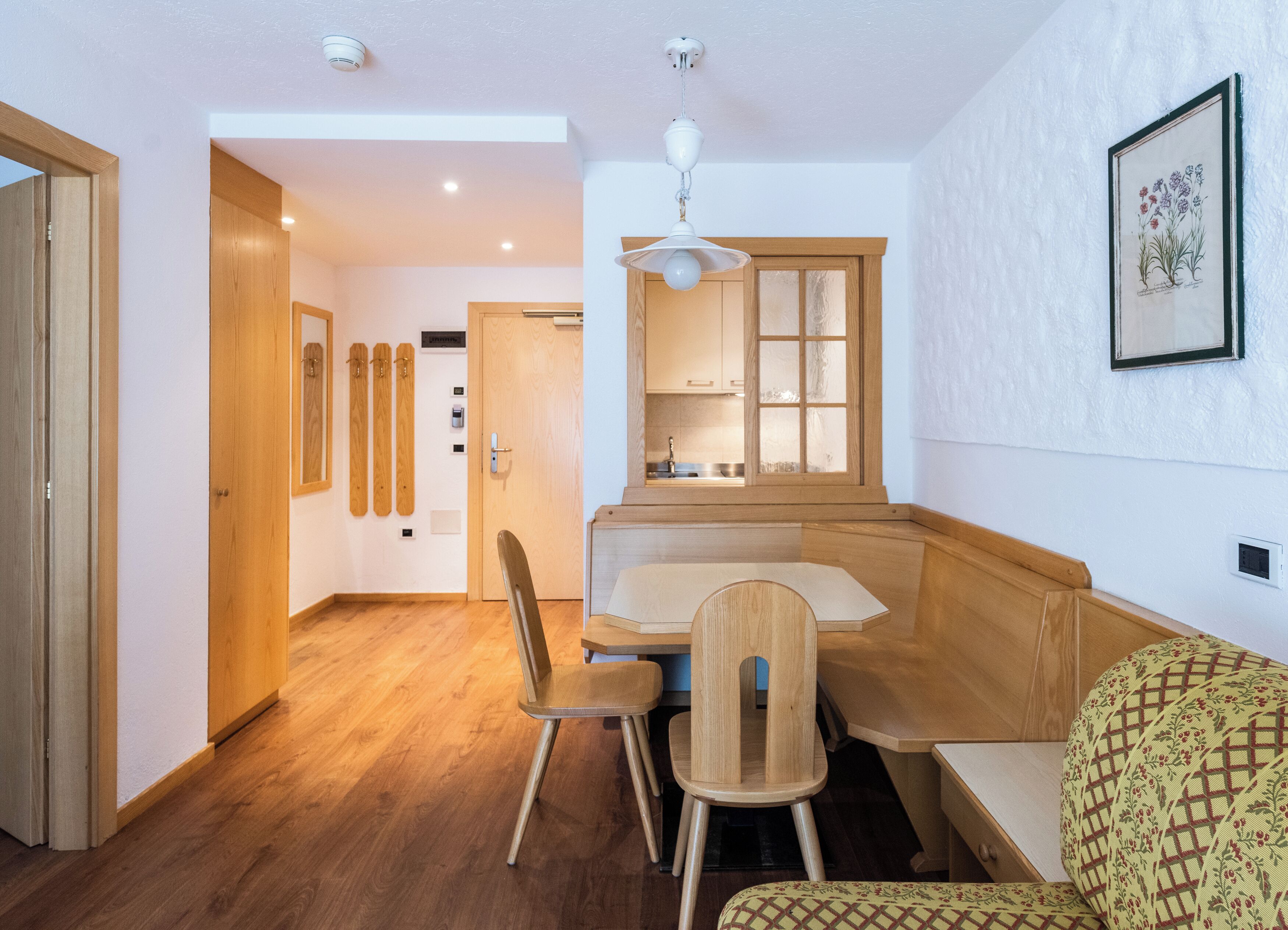 Cocina compacta con armarios de madera, una banca integrada y un comedor con mesa y sillas.