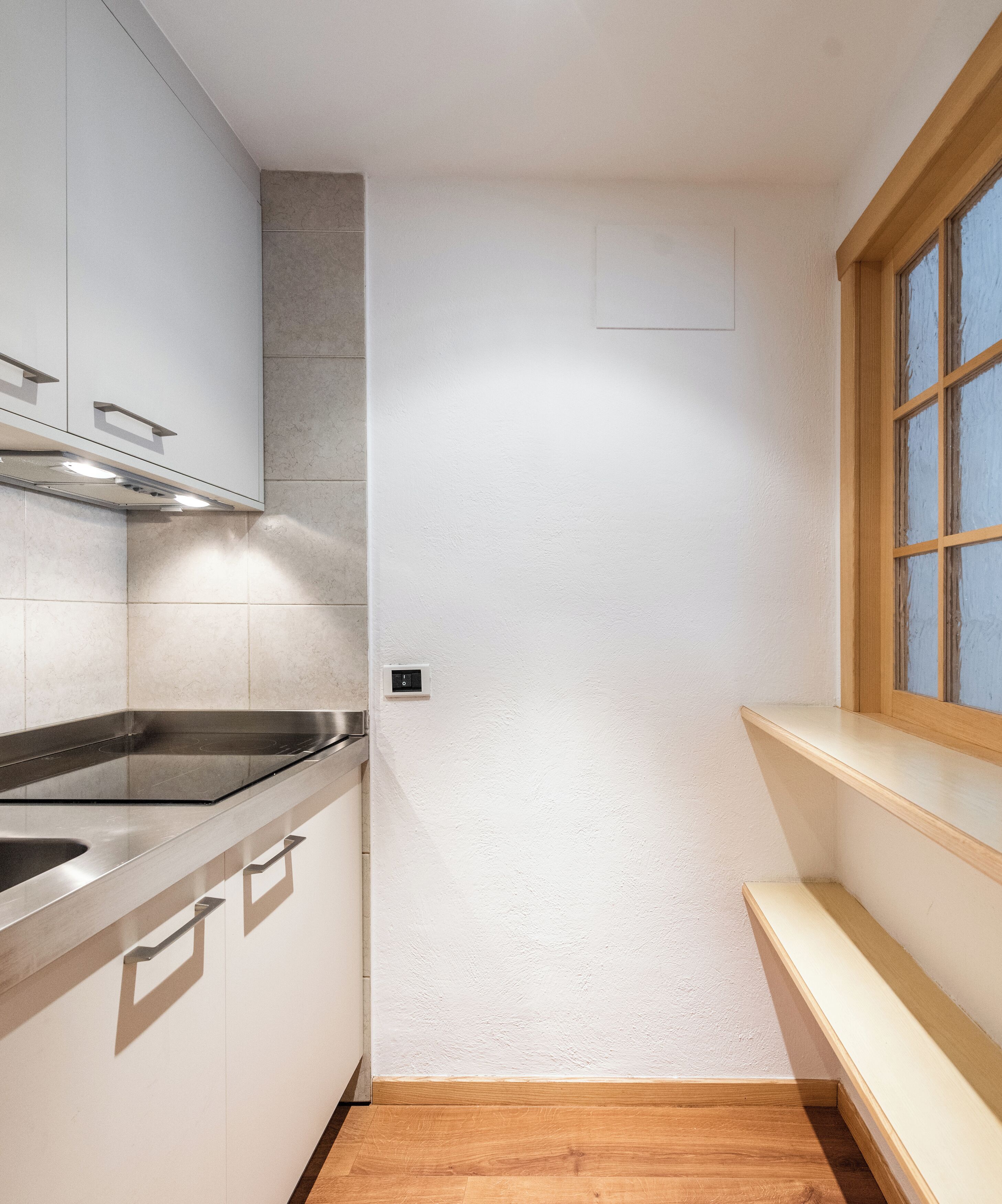 A compact kitchen with a built-in stove, a window with wooden frames, and a light switch on the wall.