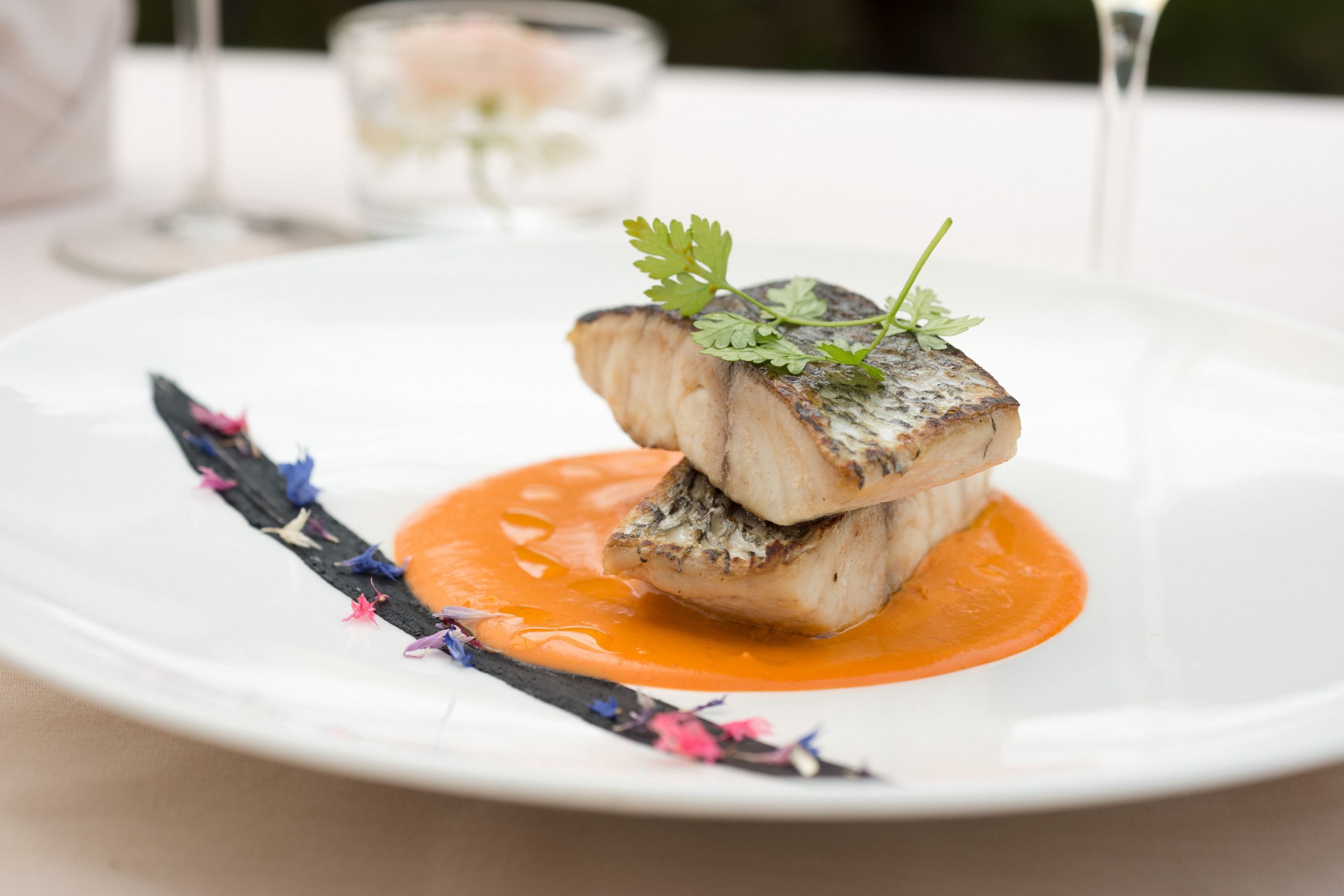 Un piatto bianco con un piatto di pesce, salsa arancione e elementi decorativi.
