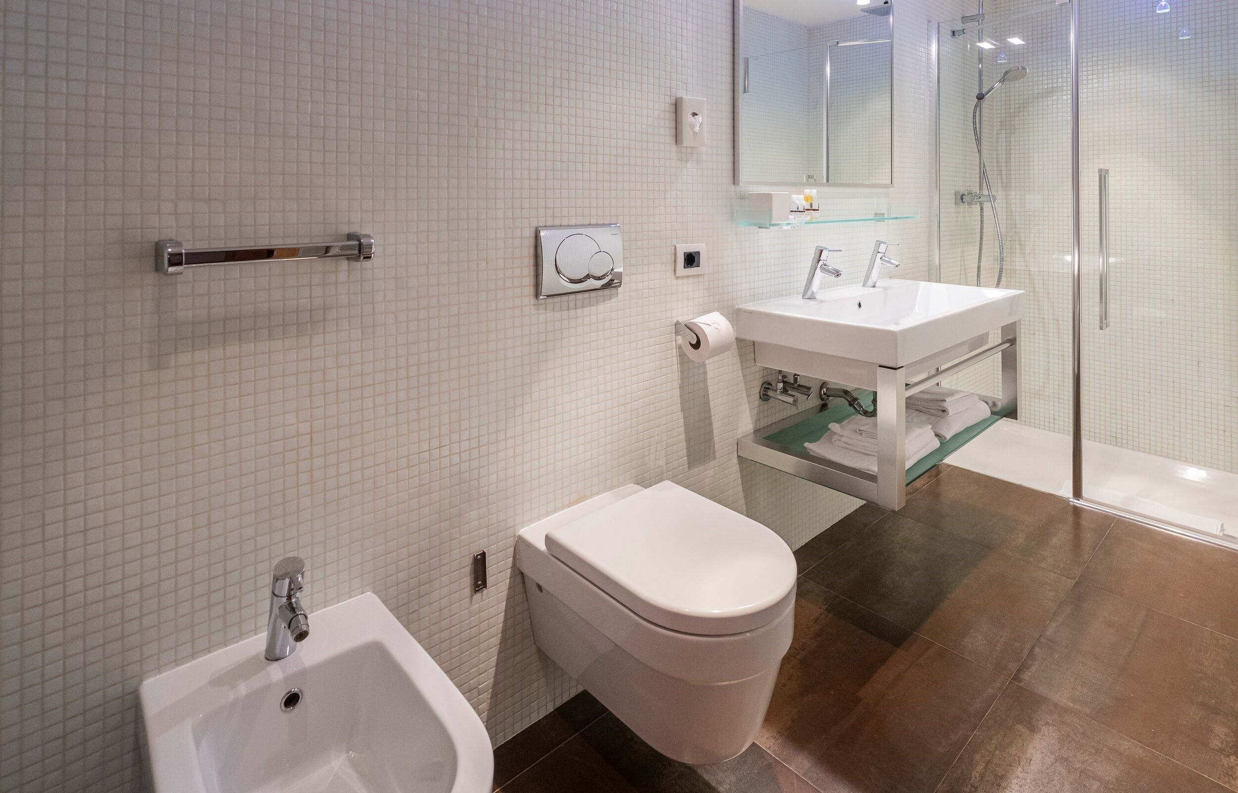A modern bathroom with a bidet, toilet, sink, and glass-enclosed shower.