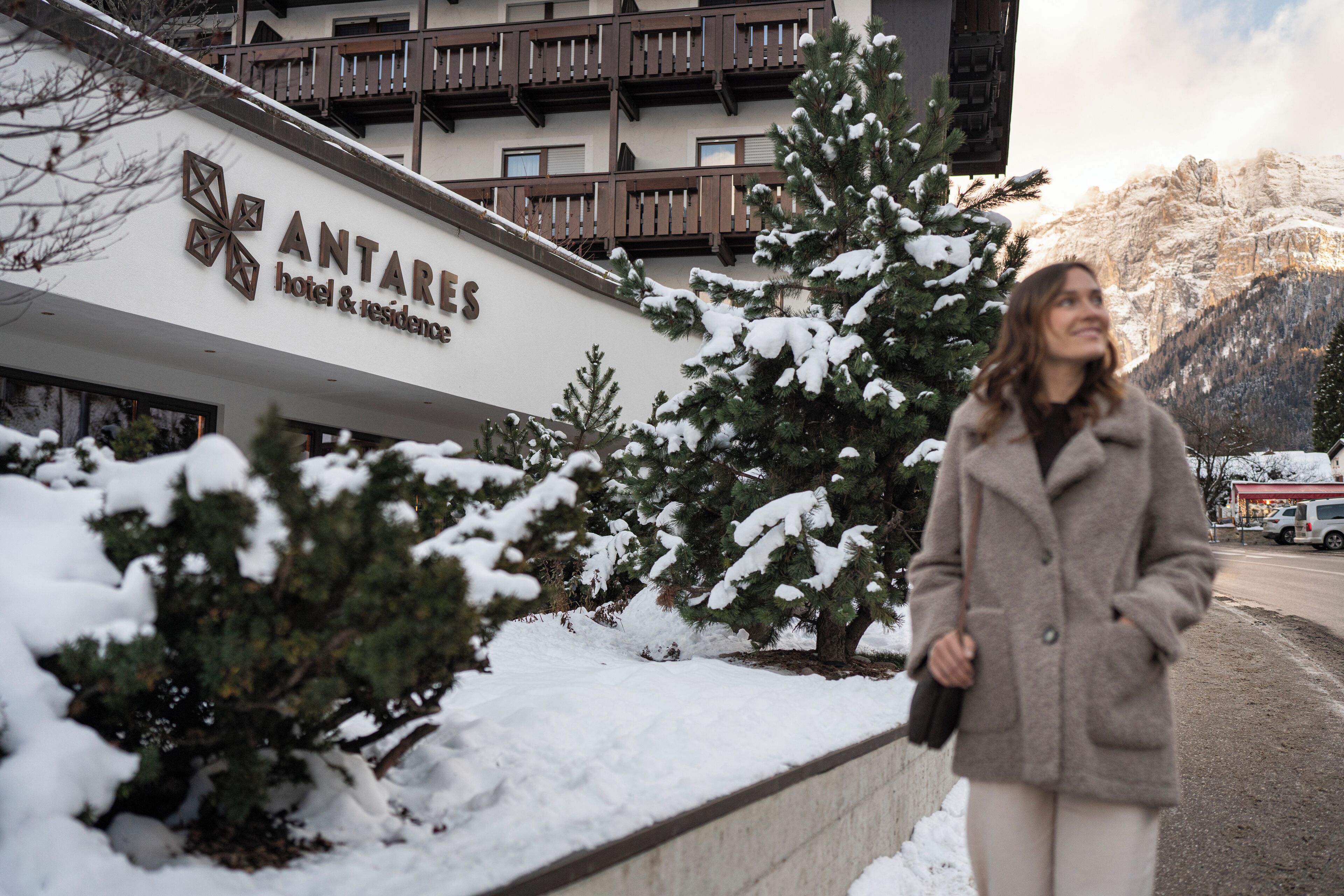 Segnaletica di un hotel con la scritta 'ANTARES hotel & residence' e sullo sfondo alberi e montagne innevate.