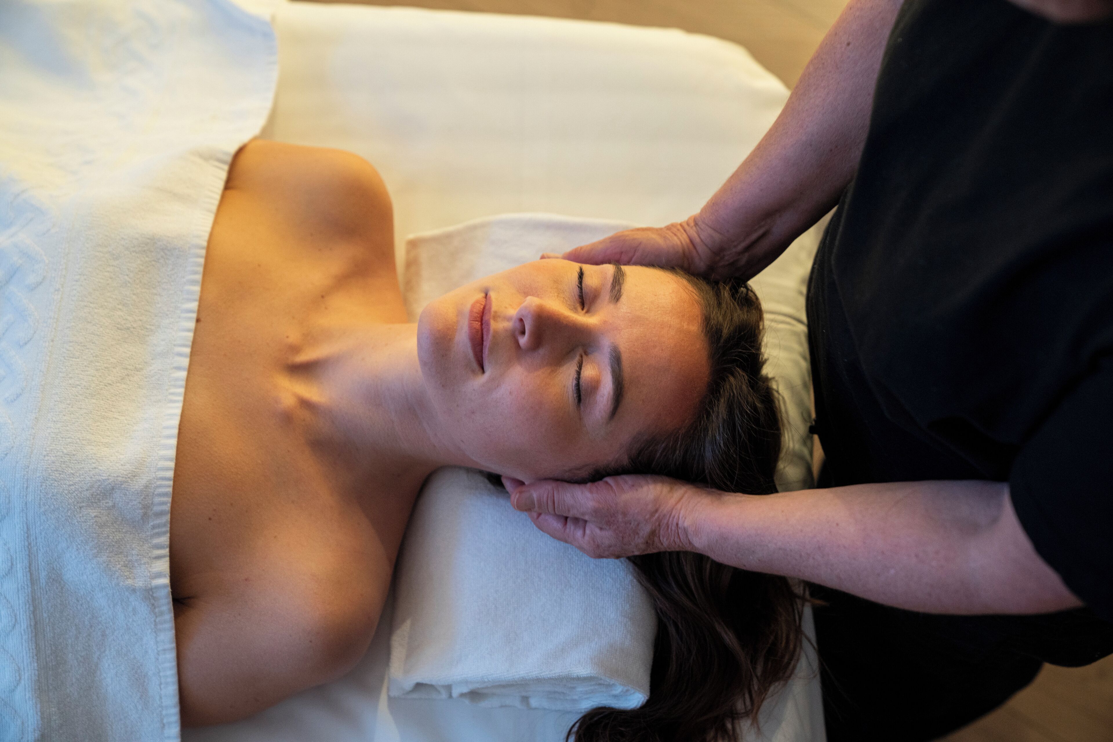 A person lying on a bed with a white pillow, receiving a massage.