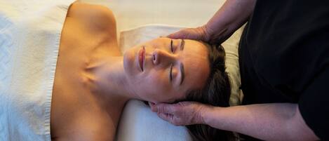 A person lying on a bed with a white pillow, receiving a massage.