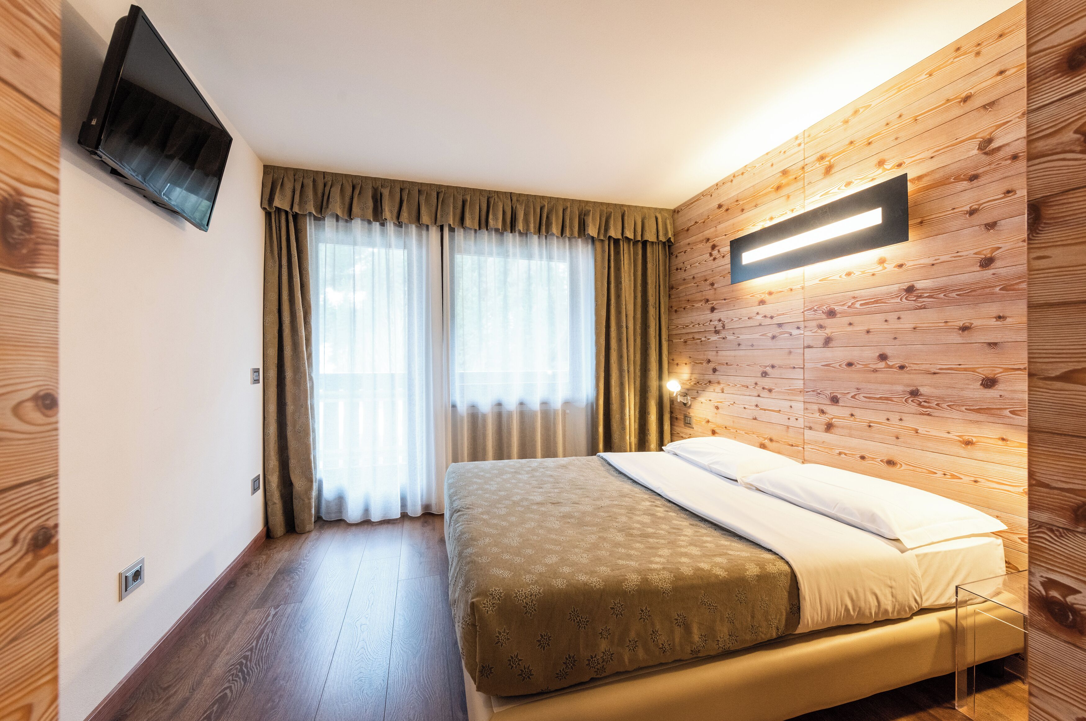 A bedroom with a bed, a TV mounted on the wall, and a wooden panel wall.