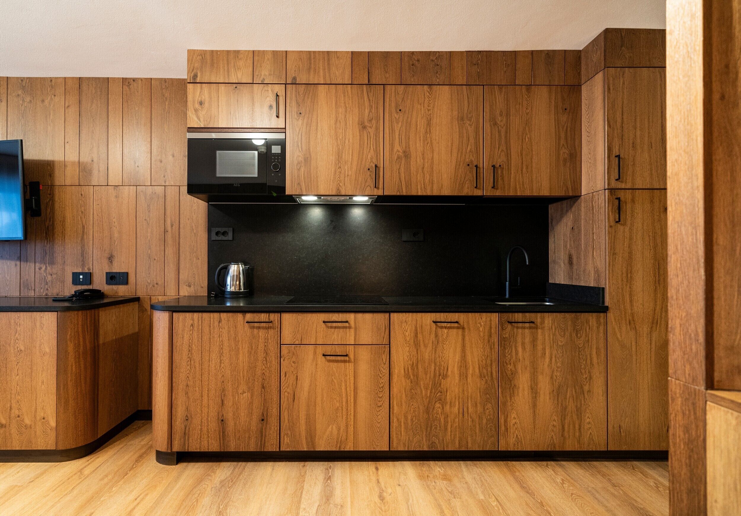 Een moderne keuken met houten kastjes, een zwart aanrechtblad en ingebouwde apparaten, waaronder een magnetron en waterkoker.