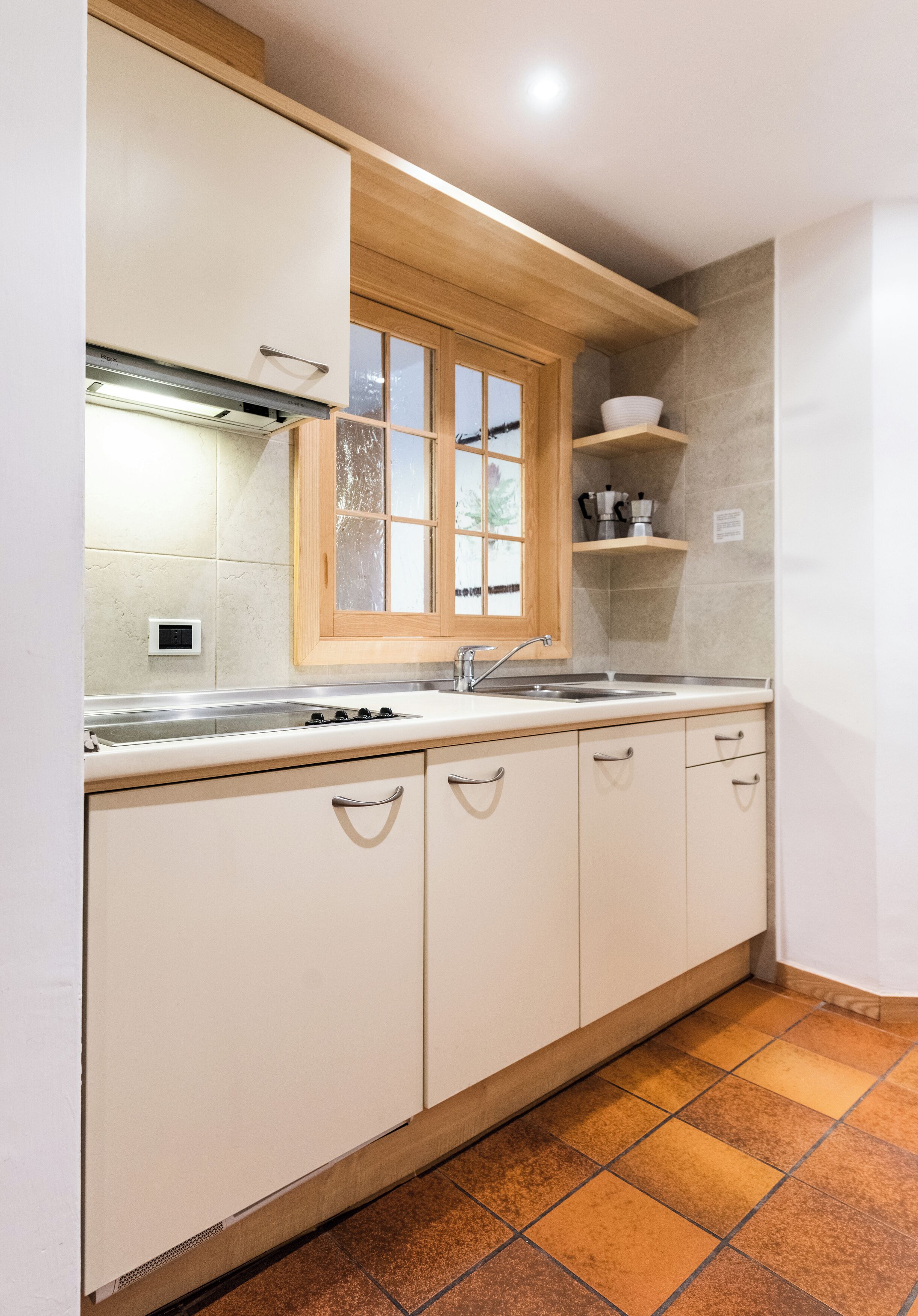 Una cocina con armarios blancos, un ventanal de madera, un lavamanos y una estufa.