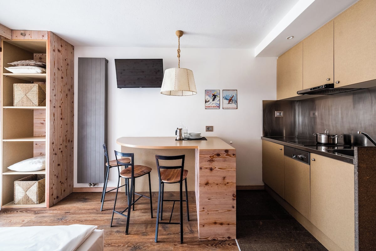 A compact kitchen with a wooden island, bar stools, a hanging light fixture, and stainless steel appliances.
