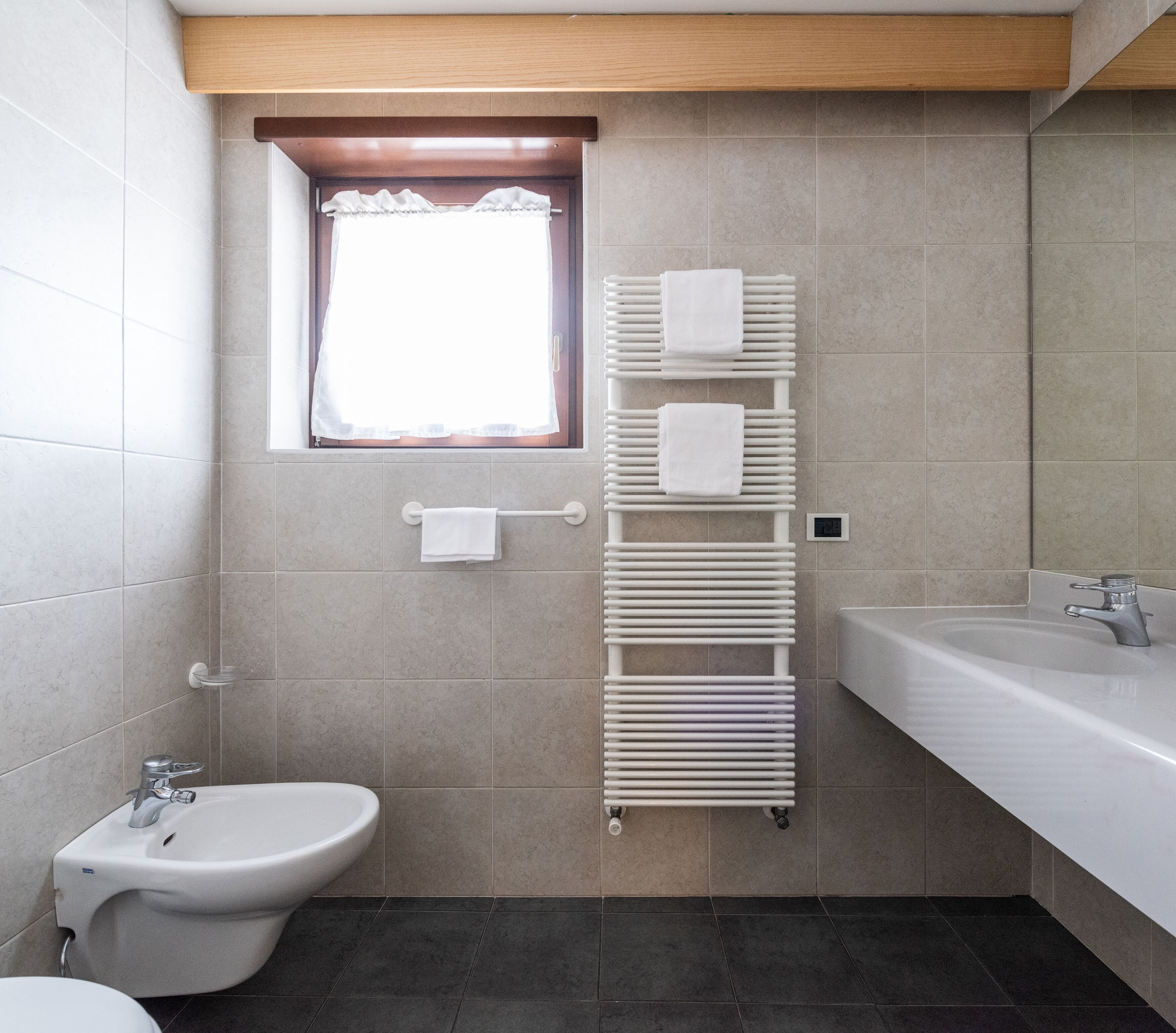 A modern bathroom with a bidet, a sink, a towel rack, and a window with curtains.