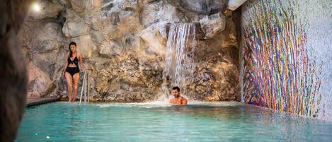 A pool with a waterfall feature and a mosaic wall.