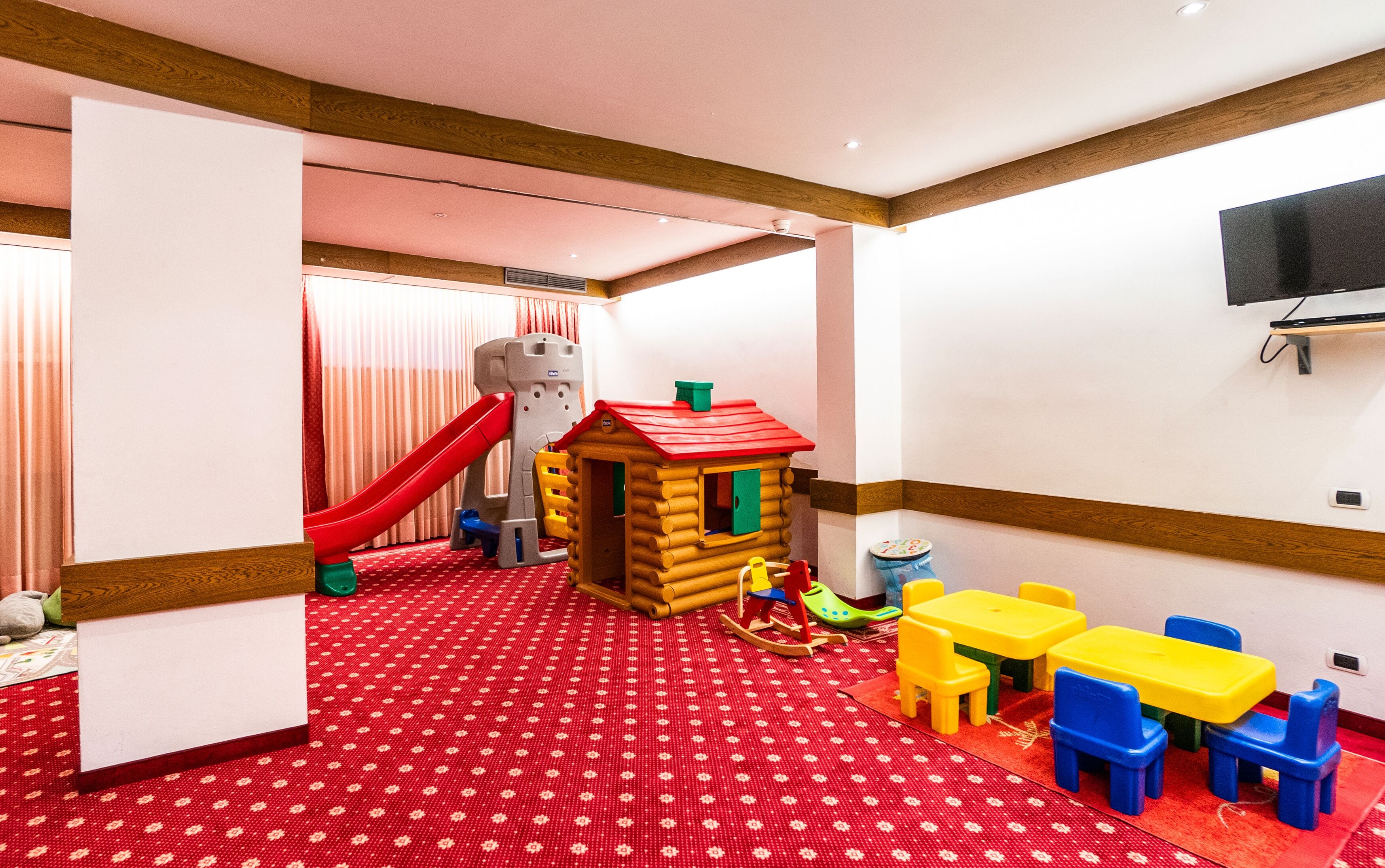 Zona de juegos infantiles con tobogán, casita de juegos y mobiliario colorido.