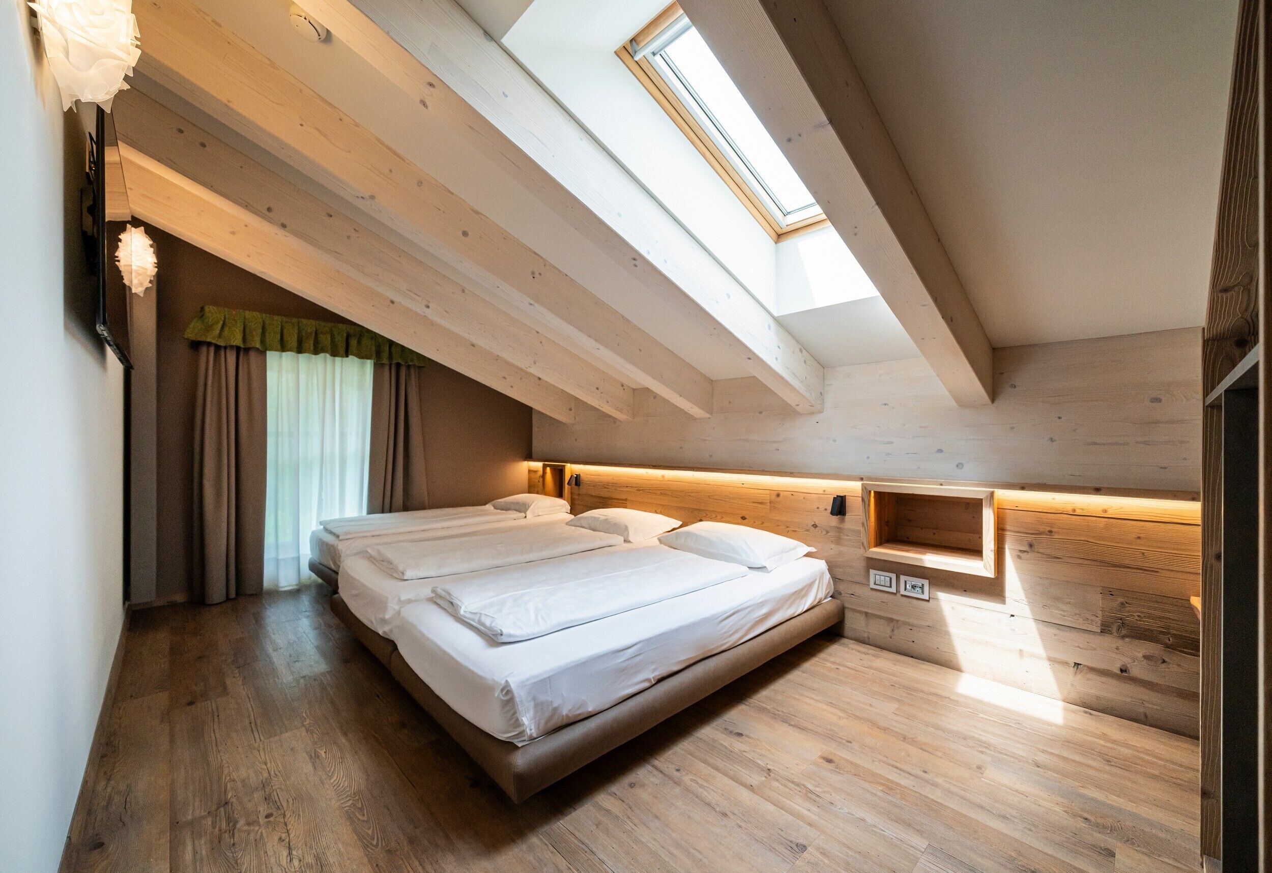 A bedroom with a skylight, wooden beams, a bed, and a bedside table.