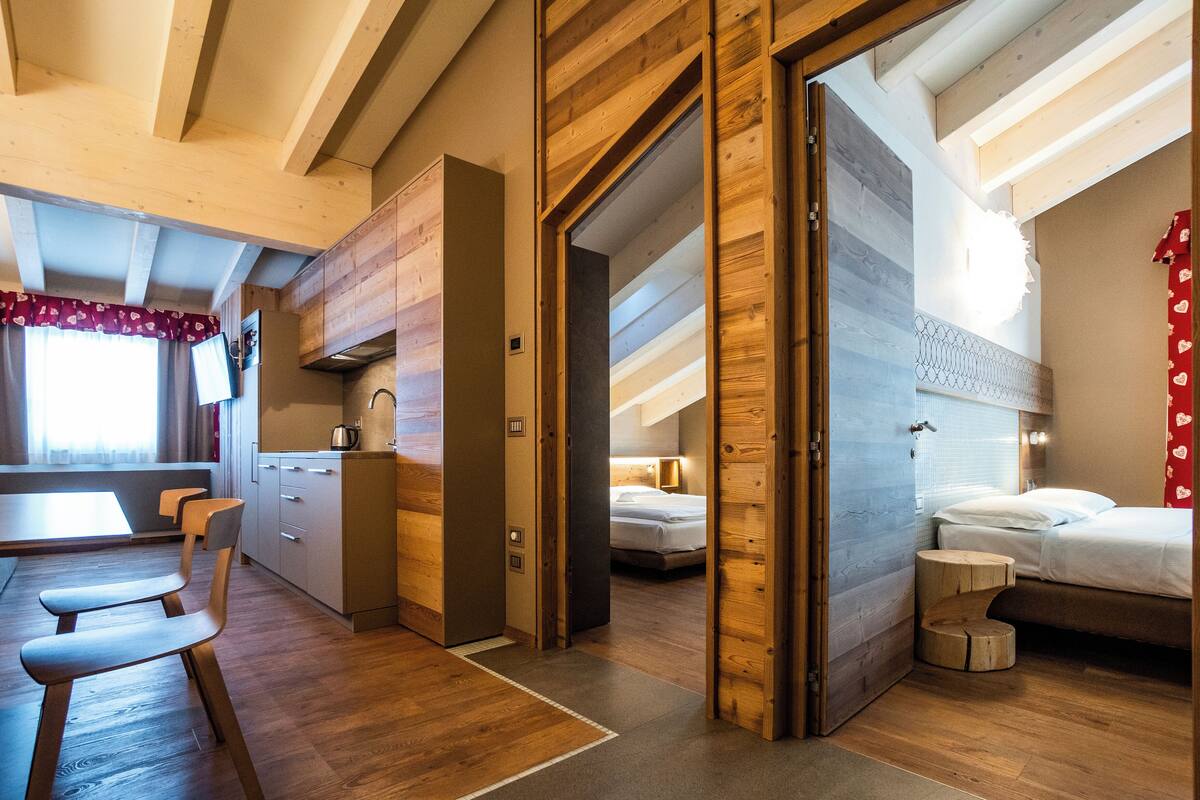 A modern hotel room with a wooden ceiling, a kitchen area, and a separate sleeping area.