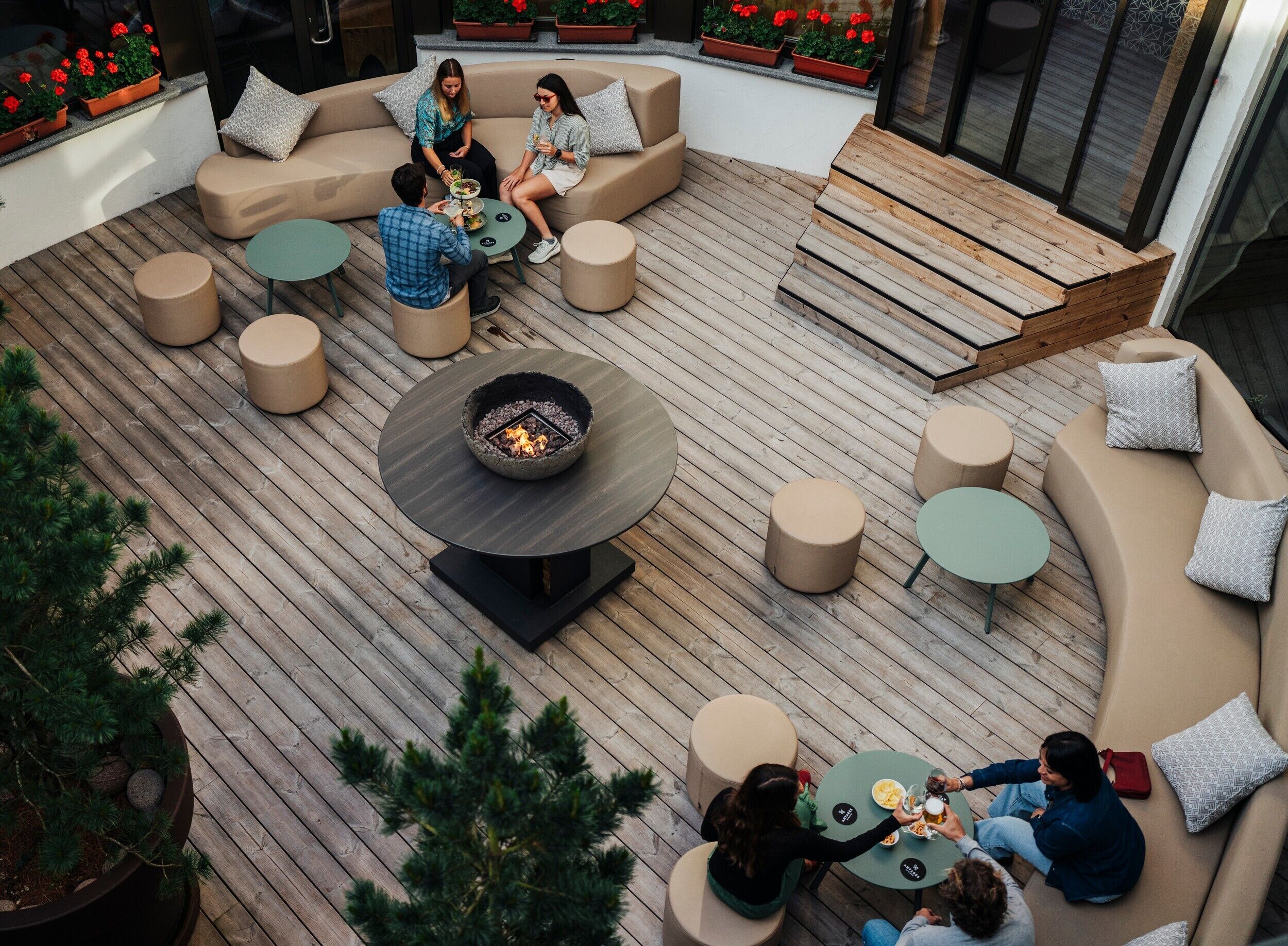 Una terraza con una chimenea, varias zonas de estar y plantas en macetas.