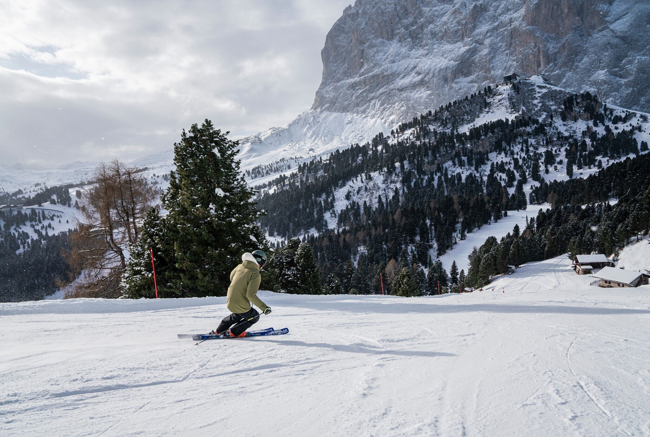 A snowy mountain landscape with a ski slope, a small cabin, and a large rocky mountain in the background.