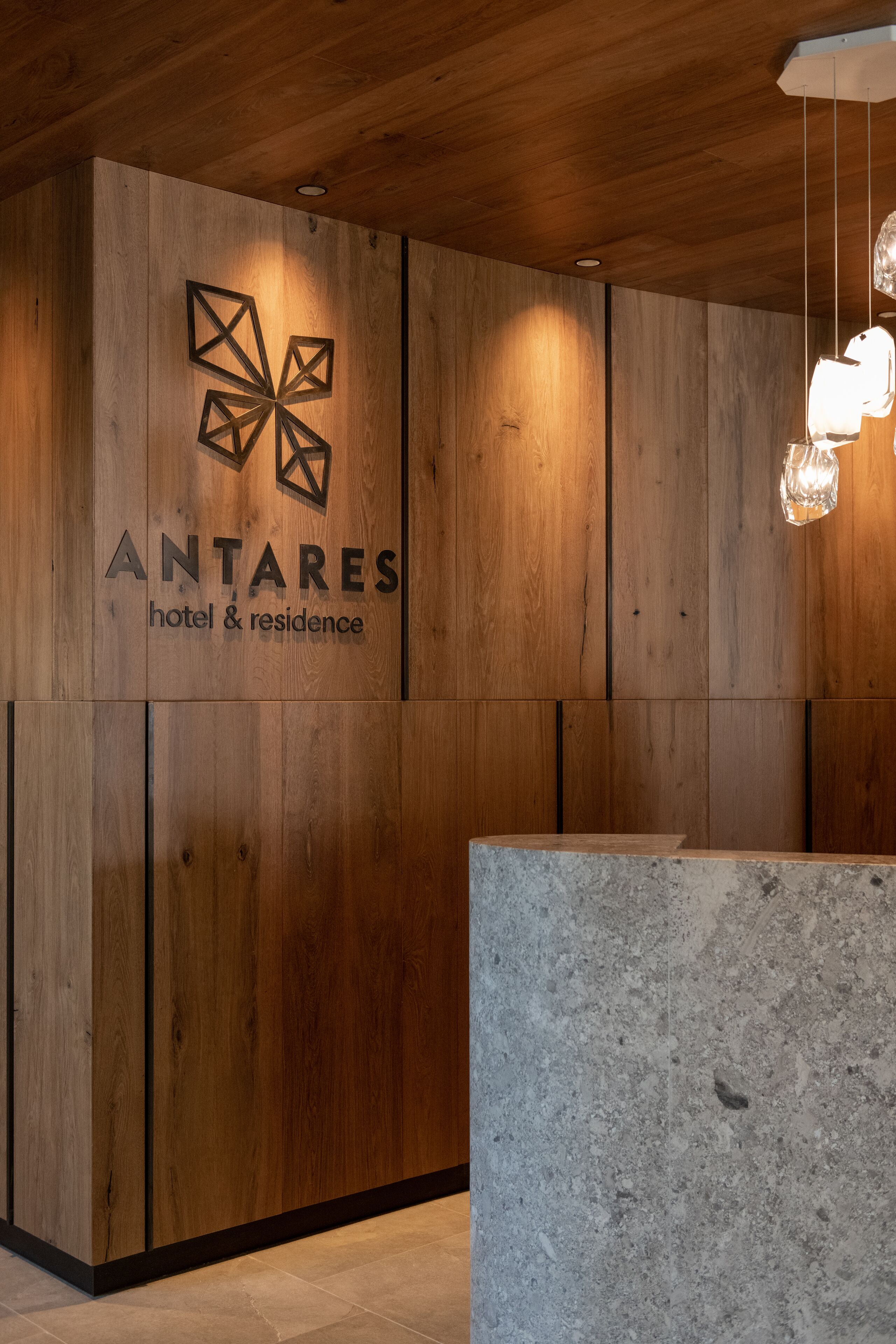 Un mostrador de recepción de madera con un logotipo y el nombre 'ANTARES hotel & residence'.