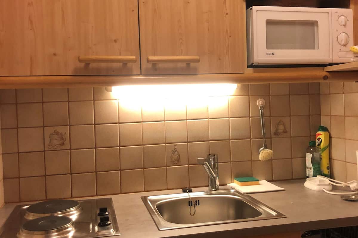 A kitchen with wooden cabinets, a stainless steel sink, a microwave, and a tiled backsplash.