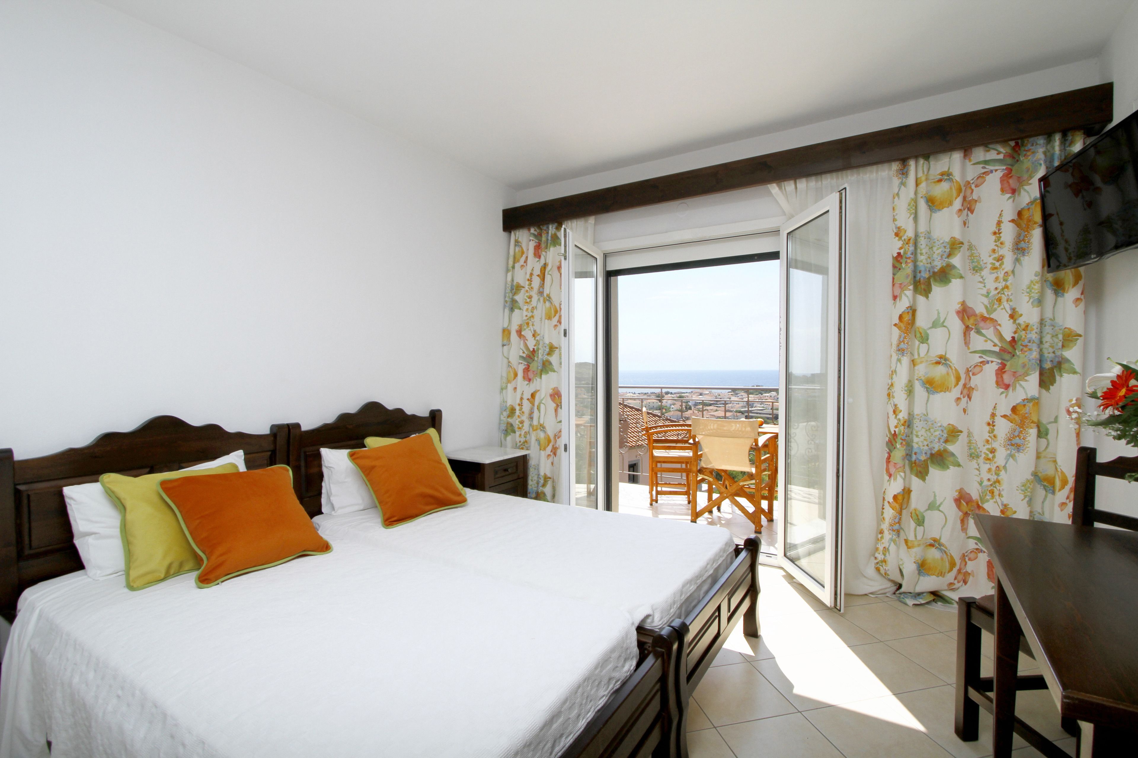 Een hotelkamer met een bed, een balkon met een tafel en stoelen, en een aan de muur bevestigde televisie.