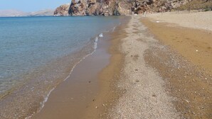 A beach with pebbly shore, clear water, and rocky cliffs. - Amygdalies Apartments (Lemnos)