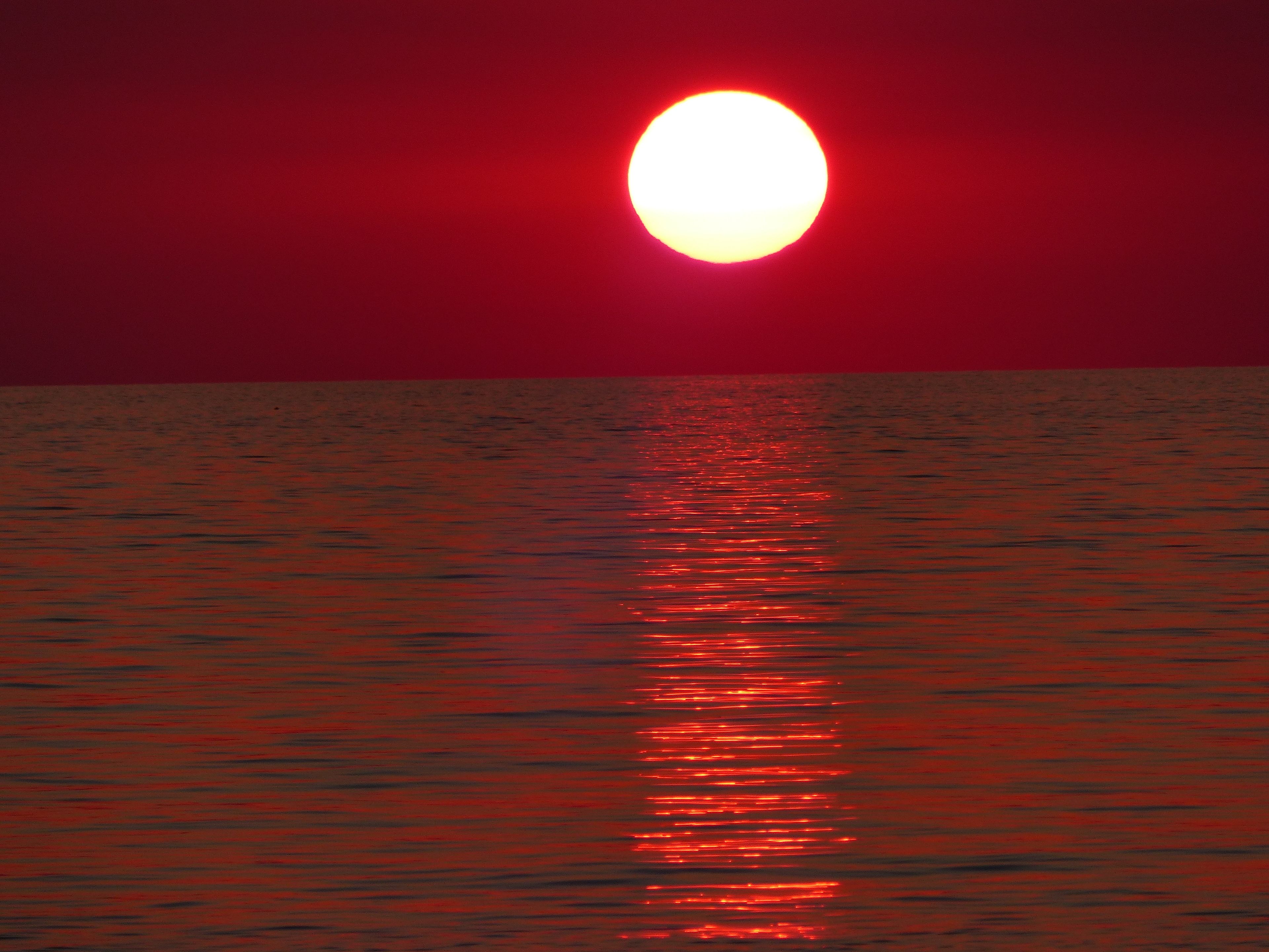 A sunset over a calm body of water with a reflection of the sun.