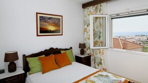 Une chambre à coucher avec un lit, des oreillers, une table de chevet, une lampe, une fenêtre donnant sur un beau paysage et un tableau encadré au mur.