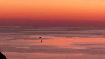 Un atardecer sobre un mar tranquilo con dos barcos a la vista.