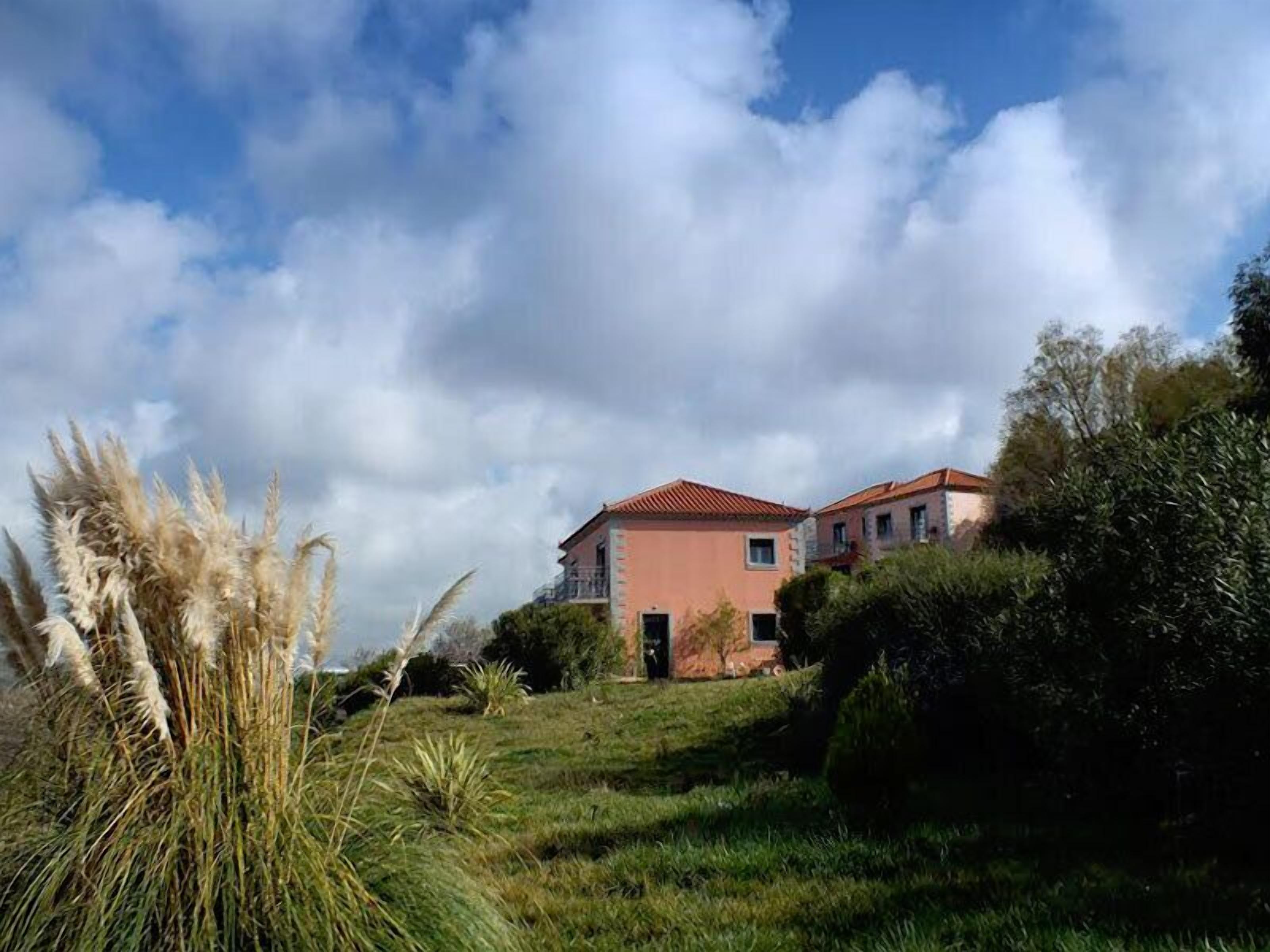 Un edificio de dos pisos con techo rojo, rodeado de follaje y pastos del pampa.