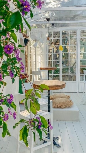 Une pièce lumineuse, avec une table et des chaises, un ventilateur et une fenêtre donnant sur un beau paysage.