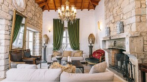 Un salon chaleureux avec un mur en pierre, un plafond en bois et une cheminée. On y trouve des fauteuils en cuir, un canapé et un lustre.