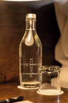 Una botella de vidrio transparente con la palabra 'PUREZA' grabada, un pequeño recipiente de vidrio y un bolígrafo sobre una superficie de madera.