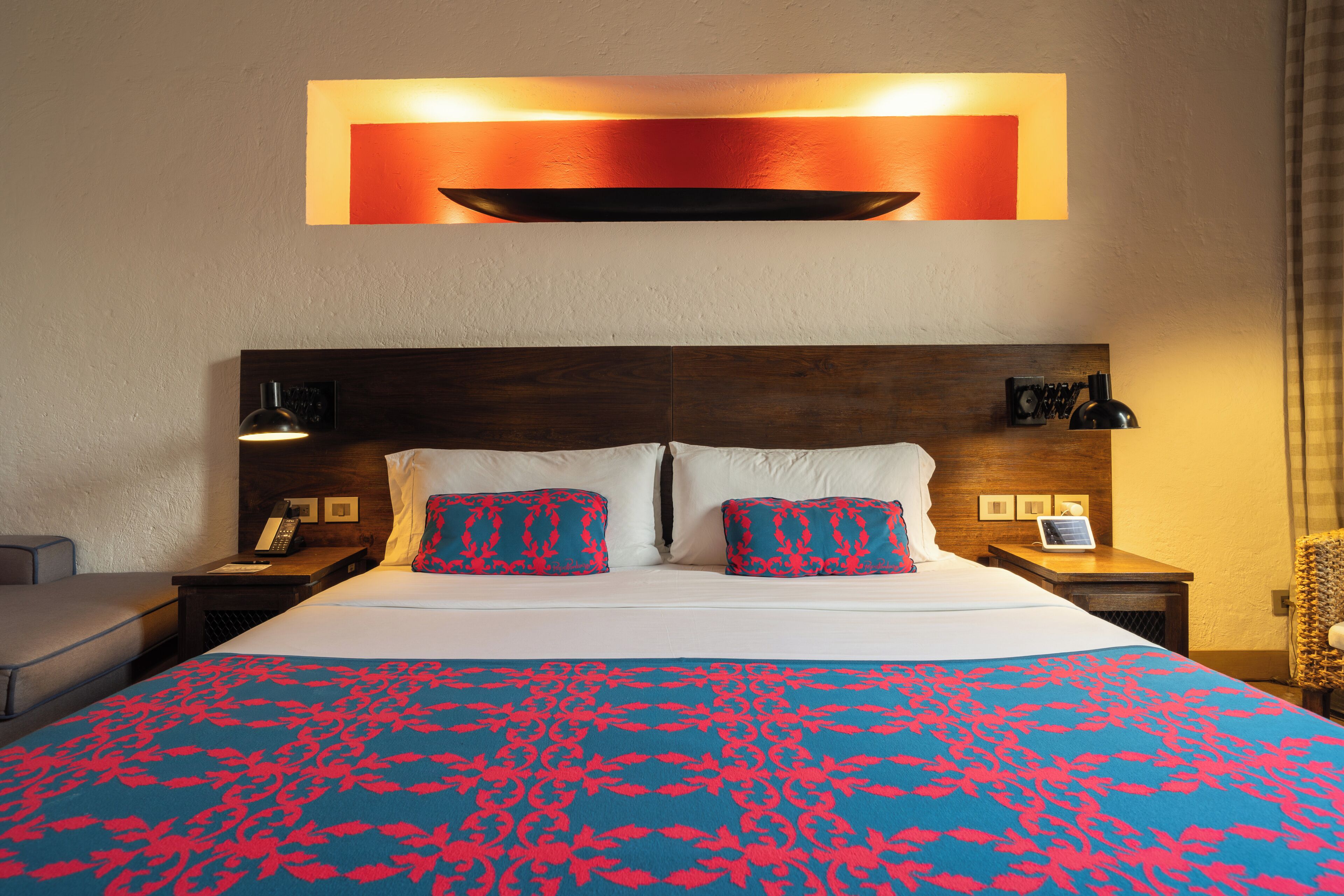 A hotel room with a large bed, two bedside tables, a desk, a chair, and a wall-mounted light fixture.