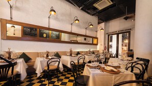 Un ristorante con pavimento a scacchi, tavoli apparecchiati con bicchieri da vino e una bacheca a parete.